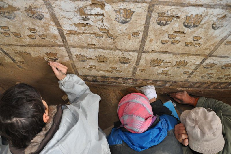 modern archaeologists clean a wall painting