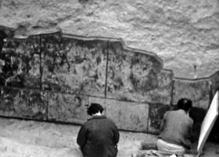 This historic photograph shows the original excavation of the Rustam cycle and two archaeologists working to reveal and document the paintings.