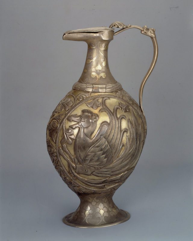 Silver ewer with slender handle. The front the body of the vase features a winged camel.